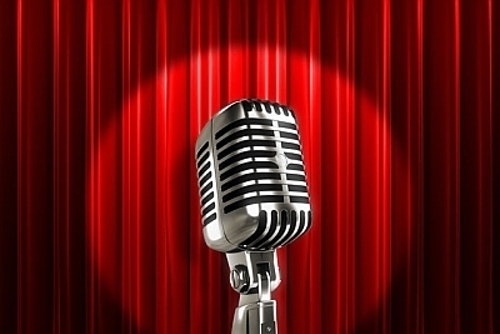 A comedian's microphone on a stage in front of a red curtain.